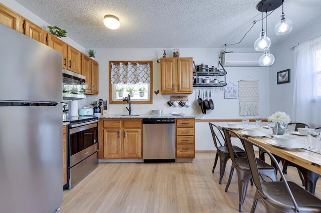 kitchen with a textured ceiling, appliances with stainless steel finishes, a sink, and light wood-type flooring