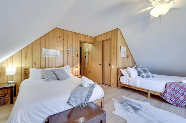 bedroom featuring a ceiling fan, wood walls, lofted ceiling, and light wood-type flooring