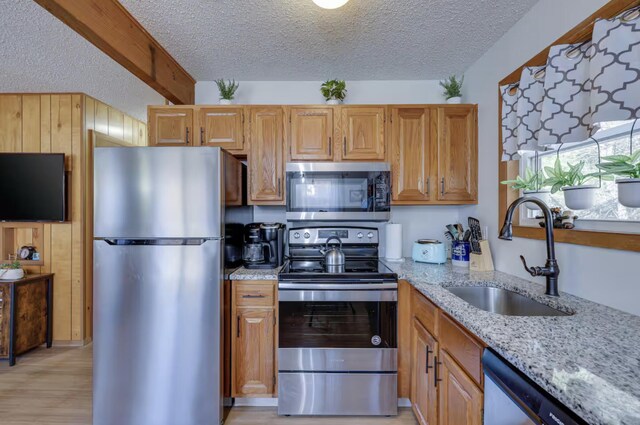 kitchen featuring a textured ceiling, appliances with stainless steel finishes, a sink, and light stone counters