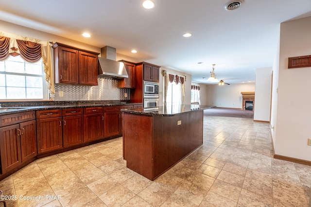 kitchen featuring oven, visible vents, stainless steel microwave, tasteful backsplash, and wall chimney range hood