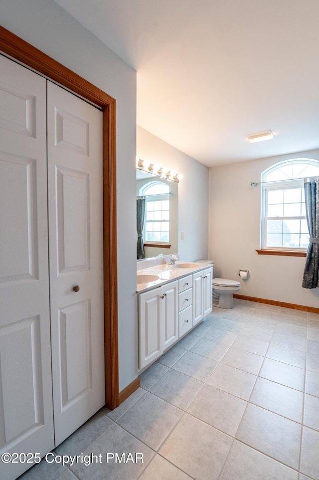 full bathroom featuring toilet, a sink, tile patterned flooring, double vanity, and baseboards