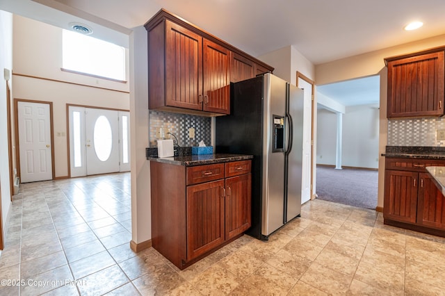 kitchen featuring dark stone counters, stainless steel fridge, backsplash, and baseboards