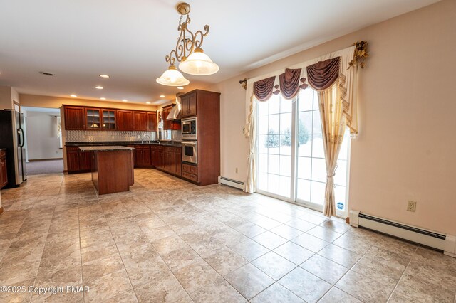 kitchen with dark countertops, a center island, appliances with stainless steel finishes, a baseboard radiator, and decorative backsplash