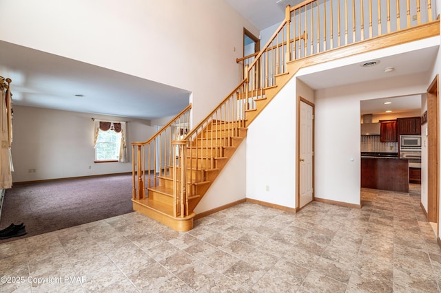 stairway with carpet flooring, a high ceiling, and baseboards