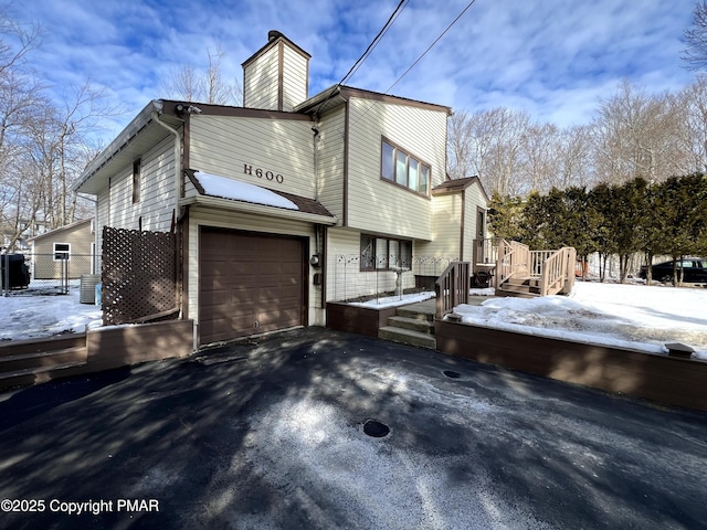 snow covered property featuring an attached garage, a chimney, and driveway