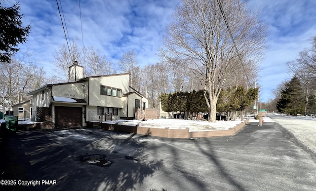 view of home's exterior with aphalt driveway, a chimney, and an attached garage