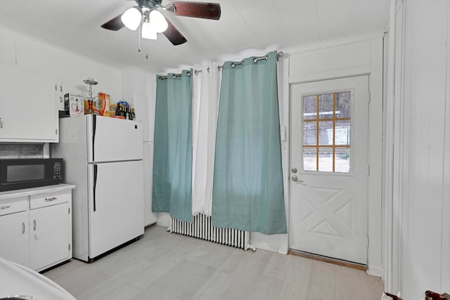 kitchen featuring radiator heating unit, black microwave, ceiling fan, white cabinetry, and freestanding refrigerator