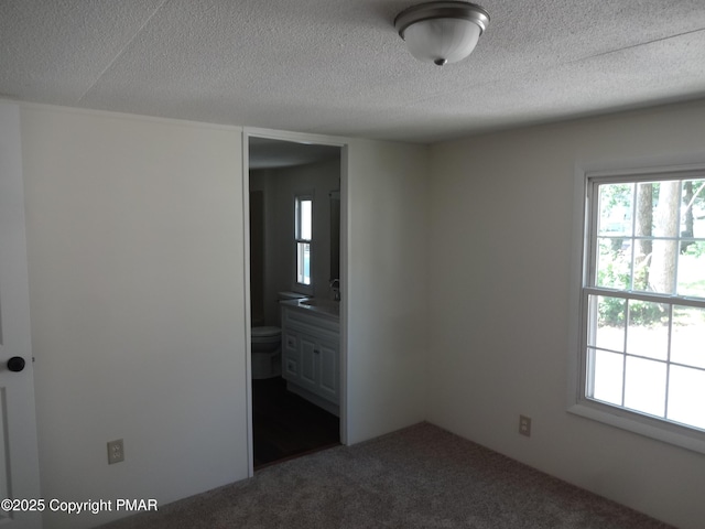 unfurnished bedroom with a textured ceiling, dark colored carpet, a sink, and ensuite bath