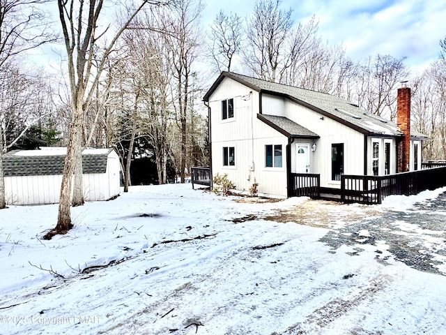 snow covered back of property with a wooden deck and a storage shed