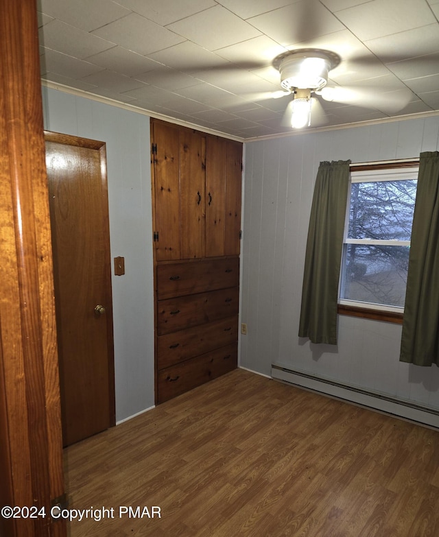 unfurnished room with a baseboard heating unit, wood finished floors, and ornamental molding