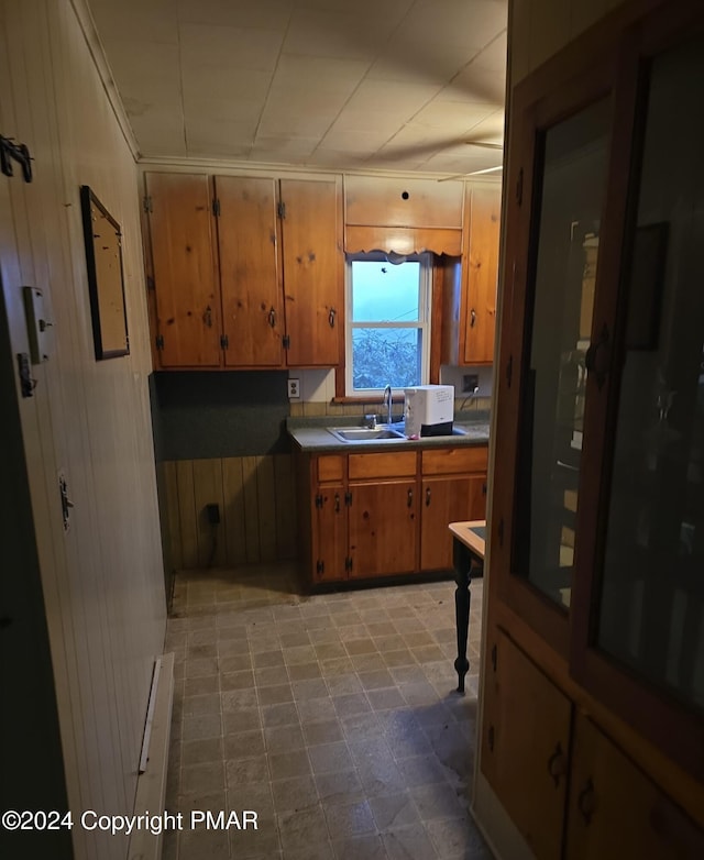 kitchen with a baseboard heating unit, wood walls, a sink, brown cabinetry, and dark countertops