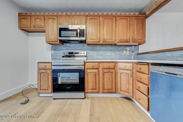 kitchen featuring stainless steel appliances, light hardwood / wood-style floors, decorative backsplash, and a textured ceiling