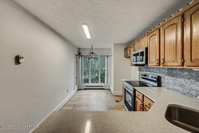 kitchen with sink, appliances with stainless steel finishes, backsplash, hanging light fixtures, and a textured ceiling