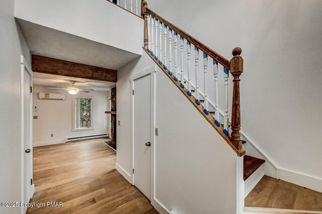 stairway featuring ceiling fan, baseboard heating, wood-type flooring, an AC wall unit, and beamed ceiling