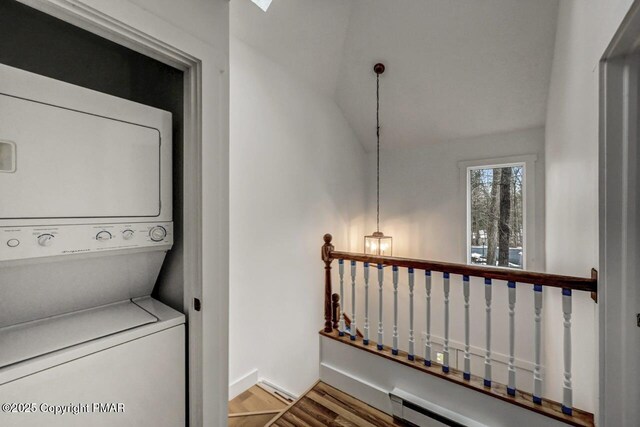 clothes washing area with stacked washer / dryer, hardwood / wood-style flooring, and baseboard heating