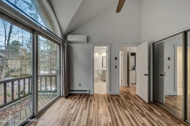 unfurnished bedroom featuring ensuite bath, a wall mounted AC, vaulted ceiling, baseboard heating, and hardwood / wood-style flooring