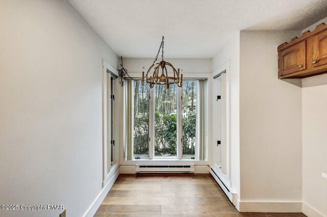 unfurnished dining area featuring a baseboard heating unit, a notable chandelier, and light wood-type flooring