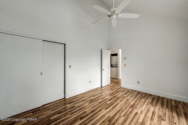 unfurnished bedroom featuring hardwood / wood-style floors, a towering ceiling, a closet, and ceiling fan