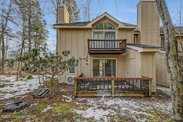 snow covered rear of property featuring ac unit and a balcony