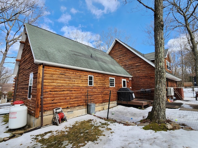 snow covered property with a shingled roof and log siding