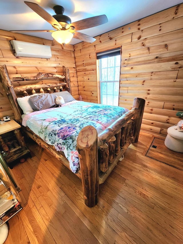 bedroom featuring rustic walls, wood-type flooring, ceiling fan, and a wall mounted air conditioner