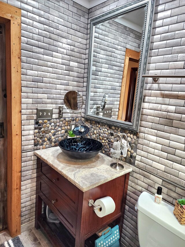 bathroom with toilet, brick wall, and vanity