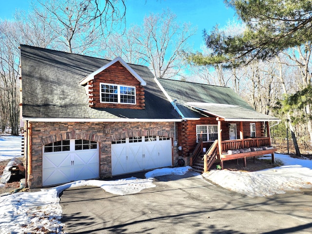 log home with a garage, stone siding, log siding, and aphalt driveway