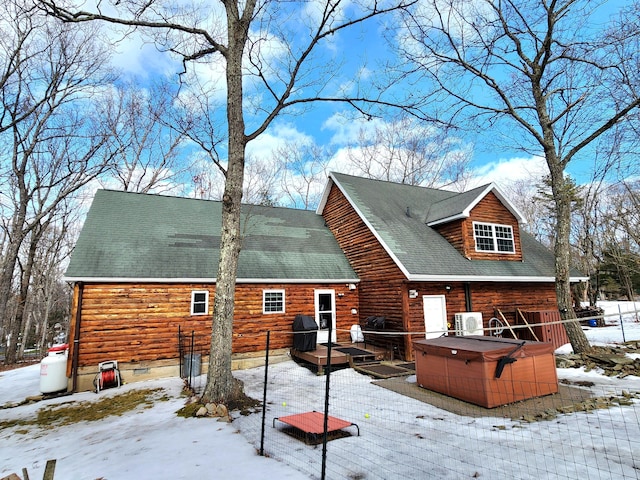 snow covered house with a shingled roof, a hot tub, and a wooden deck