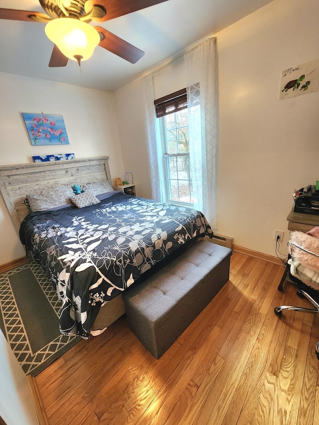 bedroom featuring a baseboard radiator, hardwood / wood-style flooring, ceiling fan, and baseboards