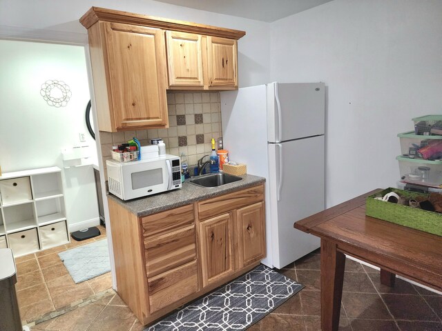 kitchen featuring dark countertops, white appliances, decorative backsplash, and a sink