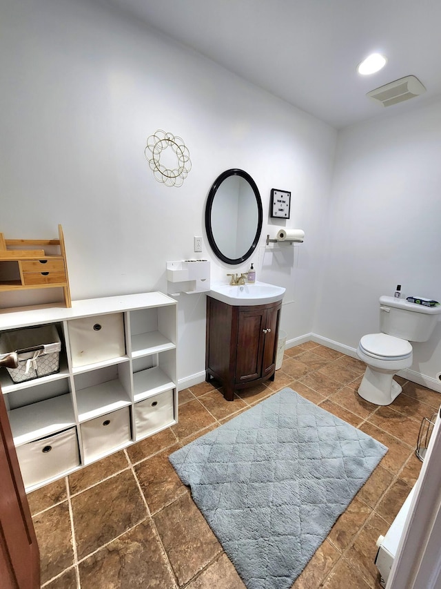 bathroom with visible vents, toilet, stone finish flooring, vanity, and baseboards