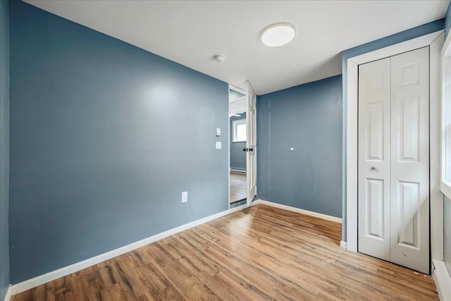 unfurnished bedroom with a closet, wood finished floors, and baseboards