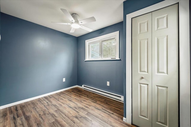 unfurnished bedroom featuring baseboards, ceiling fan, wood finished floors, a baseboard heating unit, and a closet