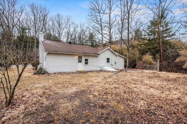 back of house with a chimney and roof with shingles