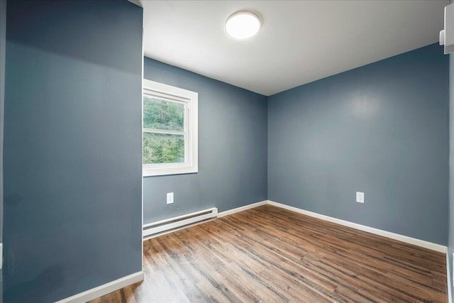 spare room featuring a baseboard heating unit, wood finished floors, and baseboards