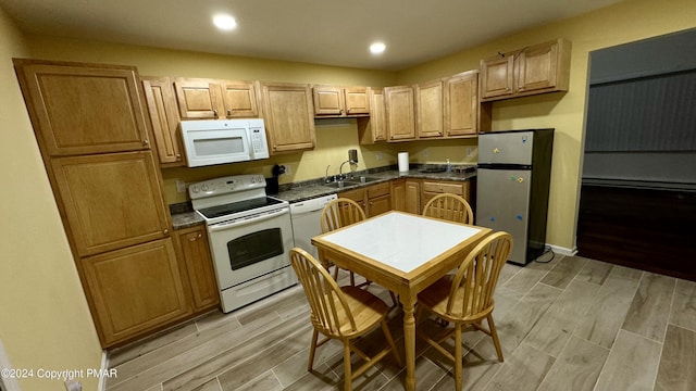 kitchen with white appliances, wood finish floors, dark countertops, and a sink