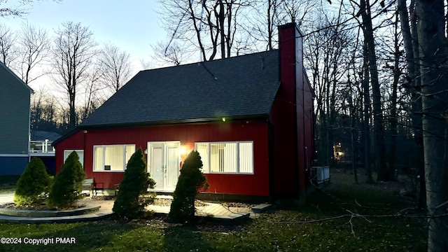 rear view of house featuring a shingled roof and a chimney