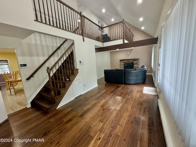 living area with high vaulted ceiling, hardwood / wood-style flooring, a stone fireplace, baseboards, and stairs