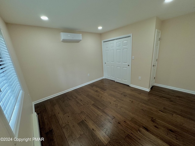 unfurnished bedroom with multiple windows, dark wood-type flooring, a wall unit AC, and a closet