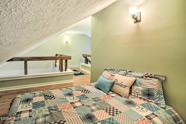 bedroom with baseboards, lofted ceiling, a textured ceiling, and wood finished floors