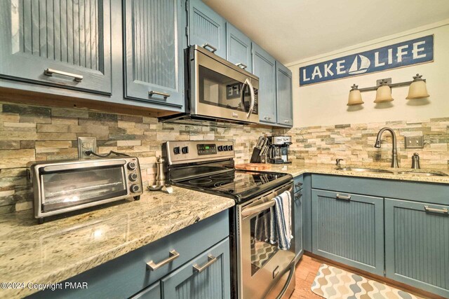 kitchen with a toaster, light stone counters, decorative backsplash, appliances with stainless steel finishes, and a sink