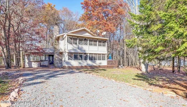 view of front of house featuring a sunroom, driveway, a chimney, and a front lawn