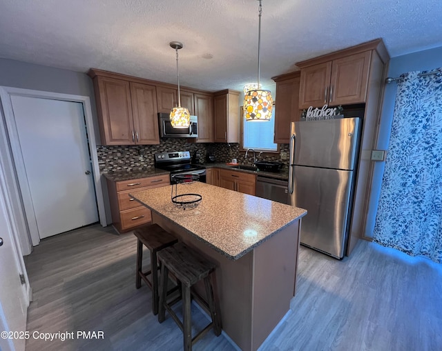 kitchen with light wood finished floors, a kitchen island, stainless steel appliances, a textured ceiling, and backsplash