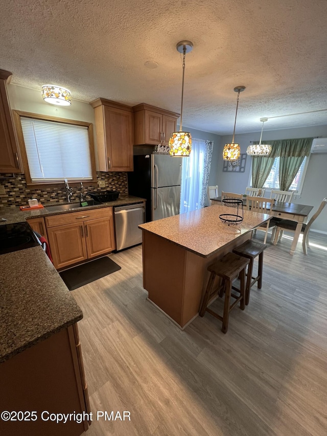 kitchen with stainless steel appliances, a sink, a kitchen breakfast bar, light wood-style floors, and decorative backsplash