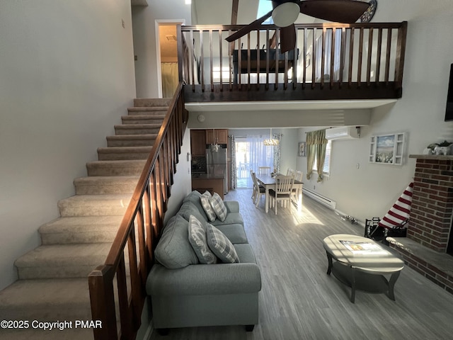 living area featuring ceiling fan, a baseboard radiator, wood finished floors, stairway, and a wall mounted air conditioner