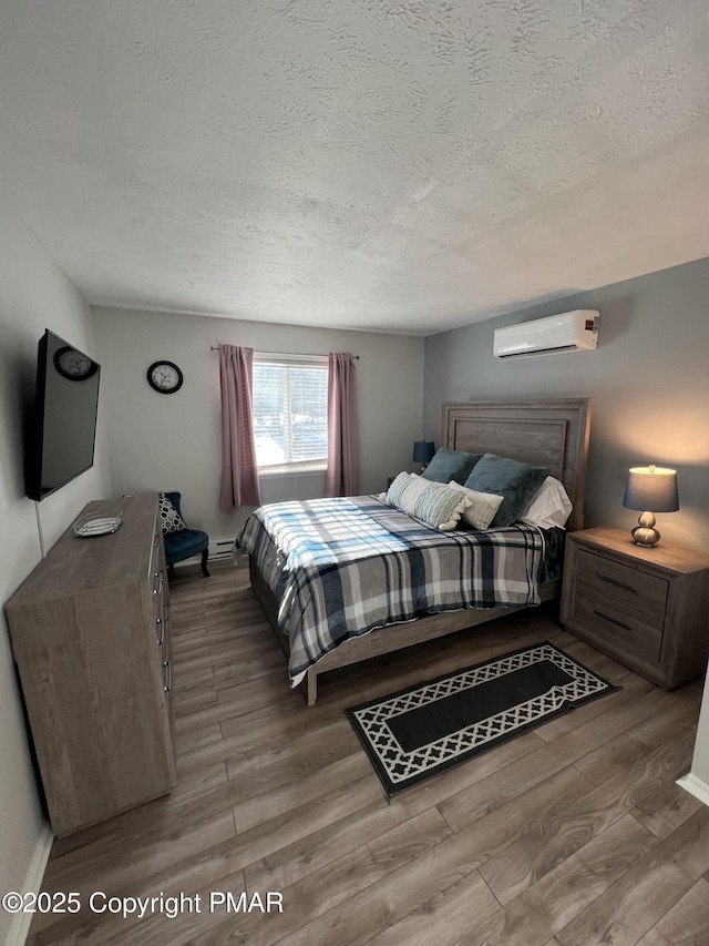 bedroom with a textured ceiling, a wall mounted AC, and wood finished floors