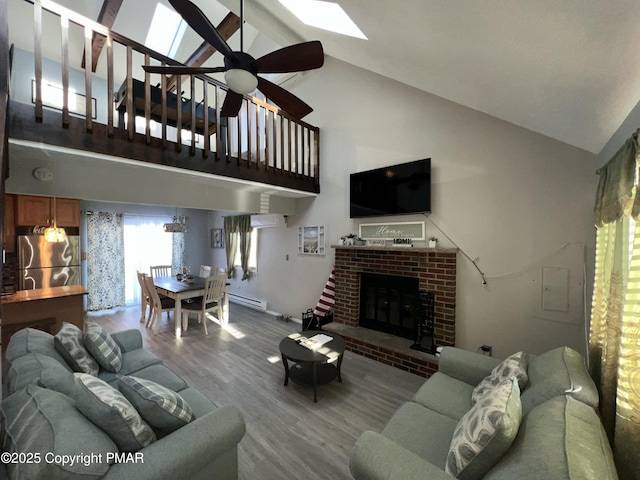 living area with a skylight, a ceiling fan, wood finished floors, baseboard heating, and a fireplace