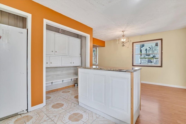 kitchen with freestanding refrigerator, baseboards, white cabinetry, a chandelier, and a wealth of natural light