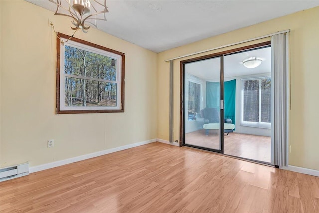 empty room featuring baseboards, a baseboard radiator, wood finished floors, and a notable chandelier