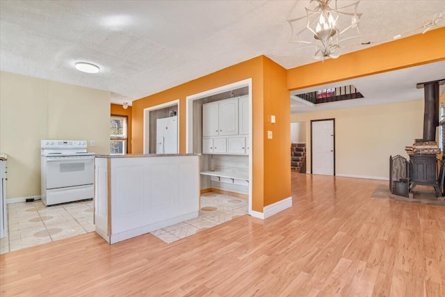 kitchen with white appliances, a textured ceiling, light wood finished floors, and a wood stove
